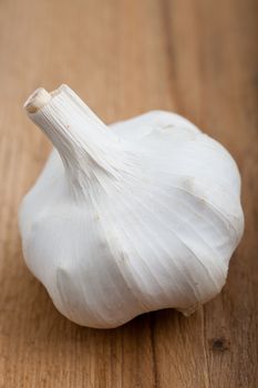 Close up view of a whole fresh garlic bulb showing the individual cloves under the papery outer skin on a wooden surface
