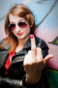 Stylish fashionable girl showing fuck off middle finger gesture against colorful graffiti wall.