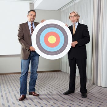 Portrait of two business colleagues holding archery target.
