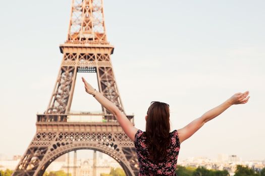 Young attractive happy woman with hands up facing the Eiffel Tower in Paris, France