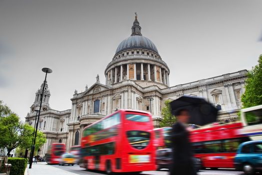 St Paul's Cathedral in London, the UK. Red buses in motion and man walking with umbrella.