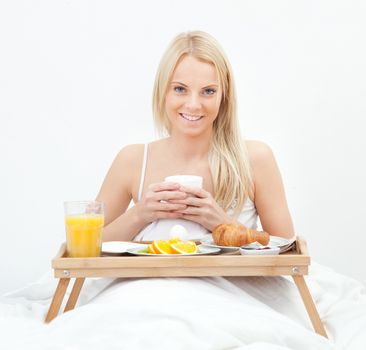 Beautiful woman drinking coffee in bed while eating breakfast