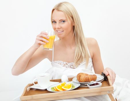 Beautiful woman drinking juice in bed while eating breakfast