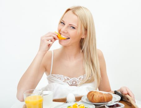 Beautiful woman eating orange in bed while eating breakfast