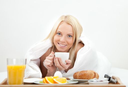 Beautiful woman drinking coffee in bed while eating breakfast