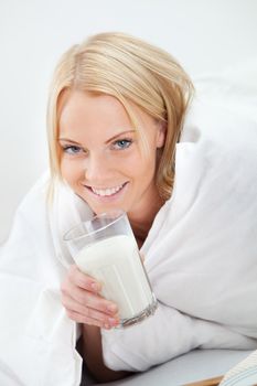 Beautiful woman drinking milk in bed while eating breakfast