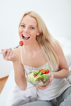 Beautiful woman eating green salad in bed
