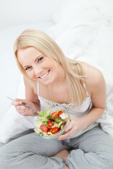 Beautiful woman eating green salad in bed