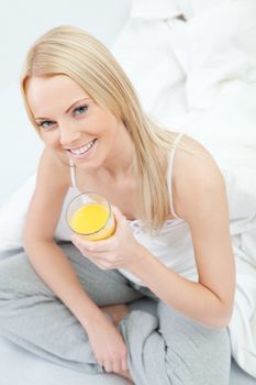 Beautiful woman drinking juice in bed while eating breakfast