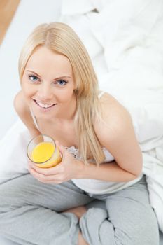 Beautiful woman drinking juice in bed while eating breakfast