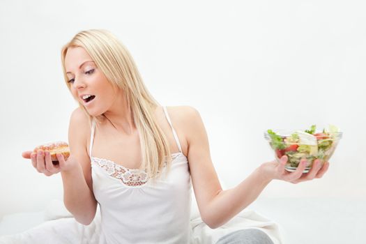 Tempted young woman making a choice between salad and donut