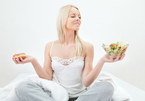 Tempted young woman making a choice between salad and donut