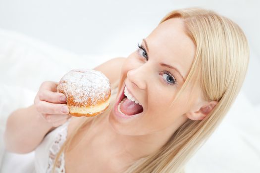 Beautiful woman eating tasty donut in bed