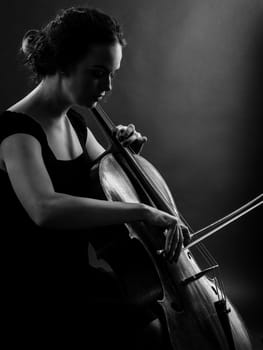 Photo of a beautiful female musician playing a cello. Backlit black and white image.

