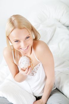 Beautiful woman eating tasty donut in bed