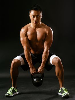 Photo of a muscular Asian man doing squats while holding a kettlebell.
