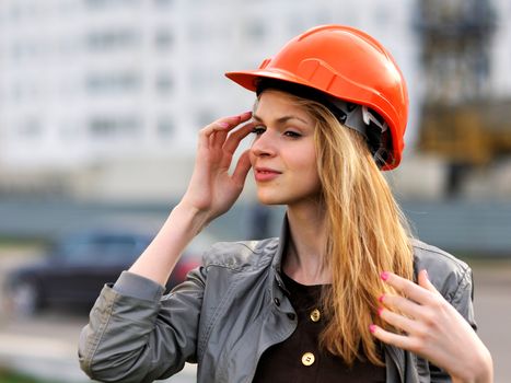 The young pleasant smiling girl with long hair costs against the building under construction