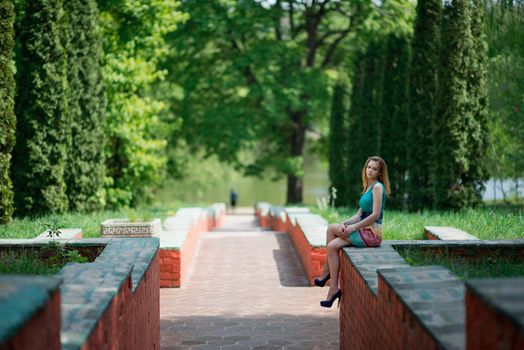 The young nice sad girl sits on a brick protection of a ladder after separation from the boy friend