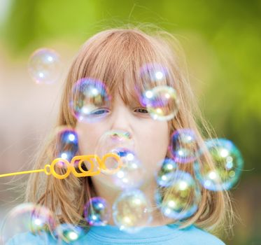 boy with long blond hair blowing soap bubbles