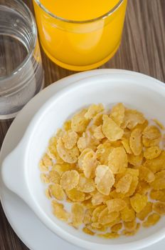 top view corn flake cereal with fresh  milk in white bowl ,  glass of  water and  juice