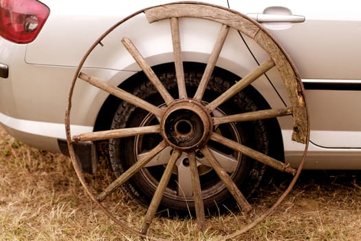 old broken wagon wheel side by new cars back