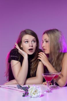 Female friends enjoying a night out sitting having cocktails at a table in a nightclub