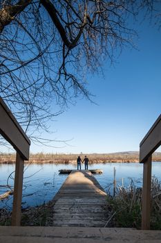 Couple standing on a wooden deck besides a lake and holding hands