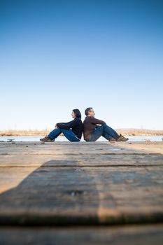 Couple sitting on a wooden deck besides a lake