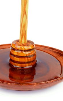 Wooden Dipper with Honey Standing into Brown Plate isolated on white background