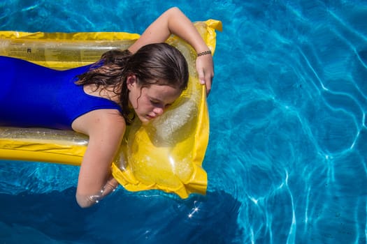 Young girl resting on yellow float lil o craft in swimming pool