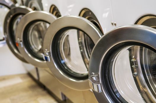 A row of industrial washing machines in a public laundromat 