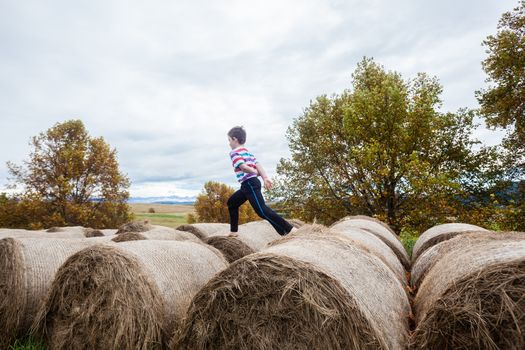 Young boy runs on top of grass bales for winter cattle feed on mountain farm