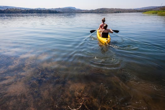 Teenage girls paddling in yellow canoe on dam  waters.