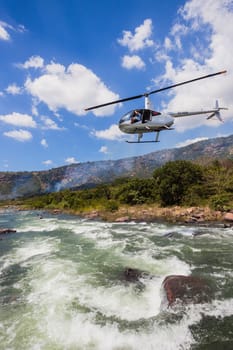 Helicopter pilot flies low over river filming canoe race of leading athlete for media coverage.