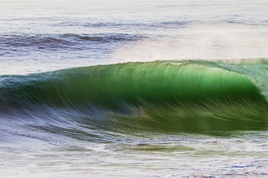 Clean shape ocean wave breaking crashing towards the sandbar shallows backlight.