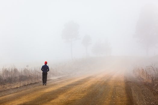 Teenager walking on a mountain dirt road in the morning mist.