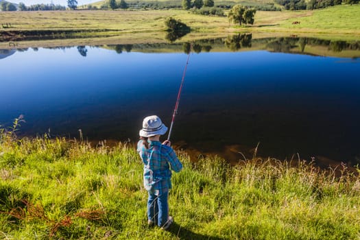 Young girl trout bass fishing in a dam with smooth glass water reflections in the mountains.