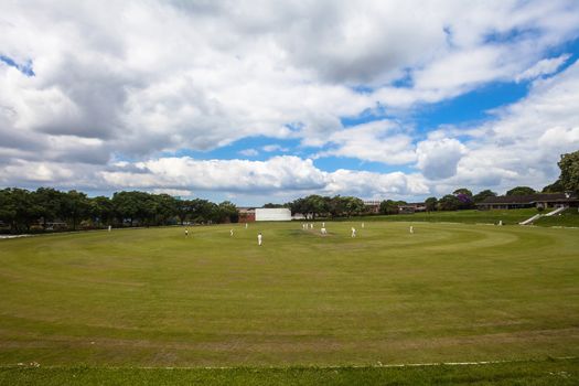 Cricket league match game with players on oval field during a summers day.