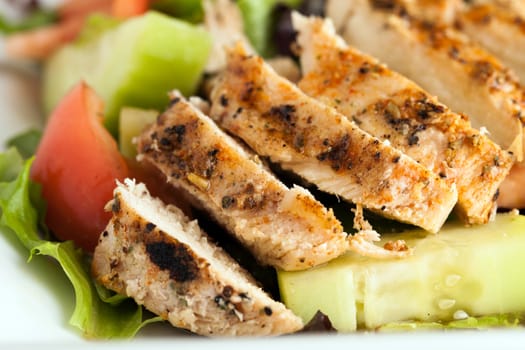 Freshly prepared grilled chicken chef style salad with tomato cucumber green pepper and romaine lettuce.