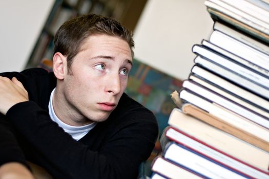 A worried student looks up at the high pile of textbooks he has to go through to do his homework assignment.