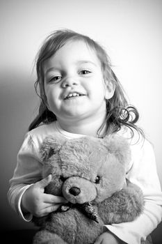Portrait of a little girl holding her favorite teddy bear in black and white.