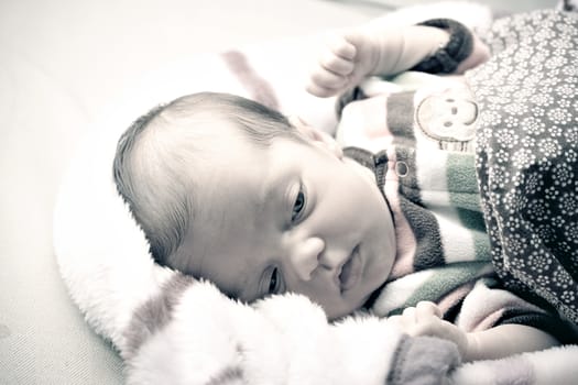 A newborn baby girl waking up from sleep and stretching under blankets.