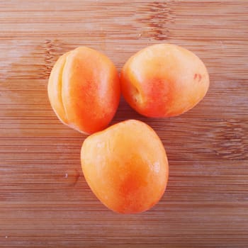 Three apricots over a lite wooden background