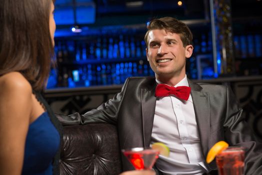 portrait of a man in a nightclub, sitting on the couch and talking with woman