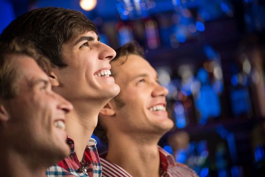 Three men stand in a row embracing smile and look in front of you, sports fans