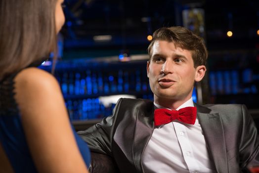 portrait of a man in a nightclub, sitting on the couch and talking with woman