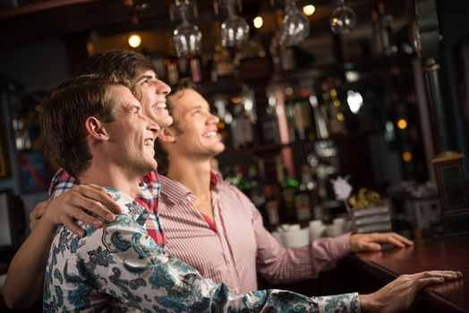 Three men stand in a row embracing smile and look in front of you, sports fans