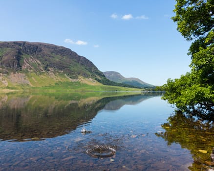 Mirror like reflection of the Lake District hills surrounding Crummock Water with a splash from thrown stone spoiling the smooth surface. Idyllic image from the English Lakes
