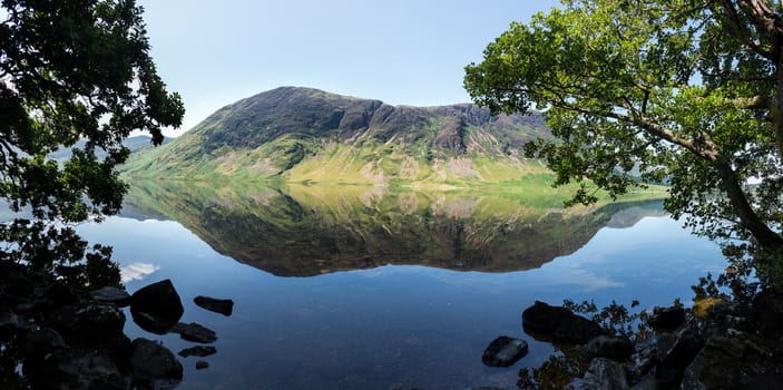 Mirror like reflection of the Lake District hills surrounding Crummock Water framed by the trees on the lakeside. Idyllic image from the English Lakes