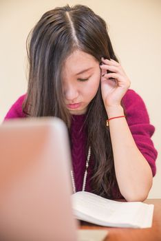 Woman reading a book behind a laptop